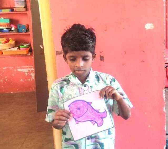 A young student holds up the pink fish he has coloured in art class