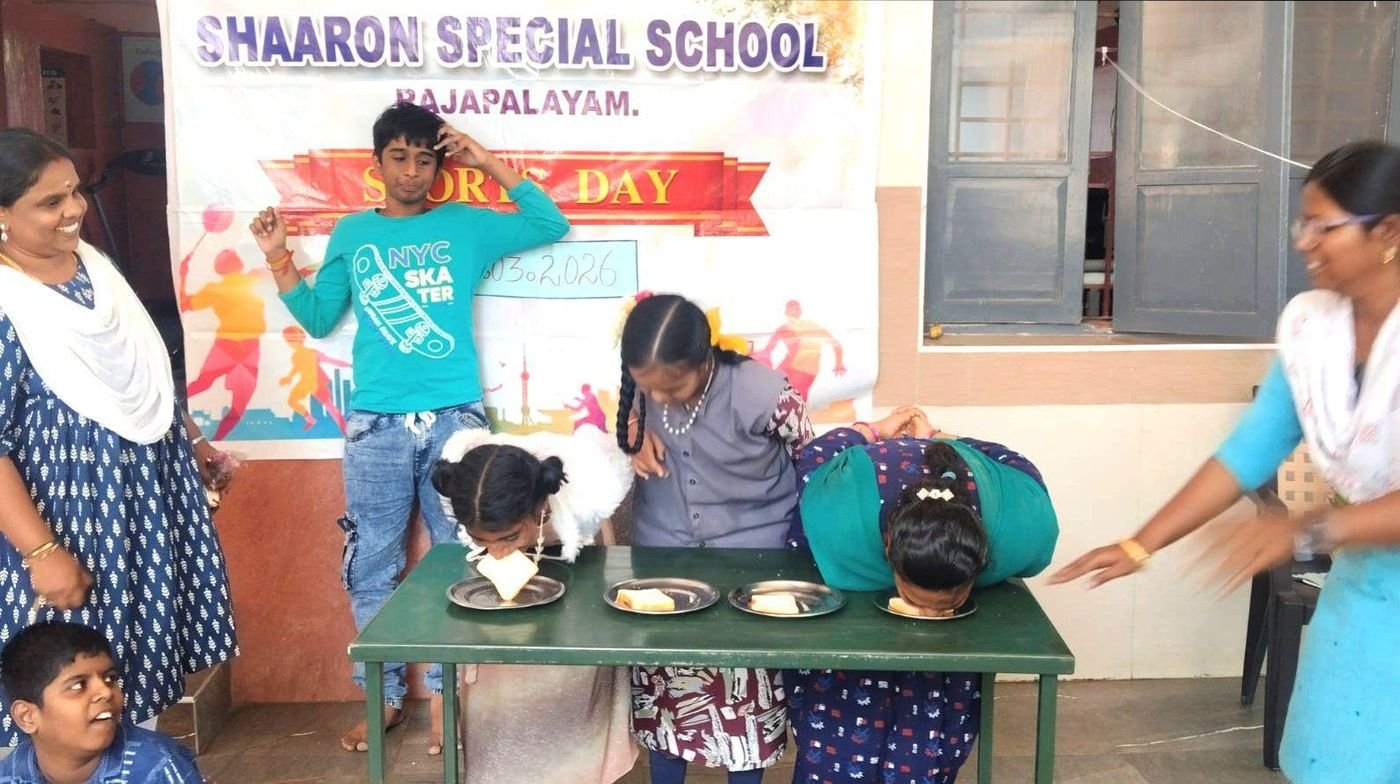Students take part in a fun eating contest at a table while teachers cheer them on at Sports Day