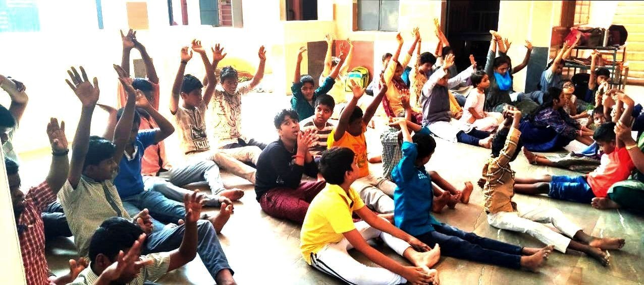 A hall full of students sitting on the floor stretching their arms up during morning warm-up exercises